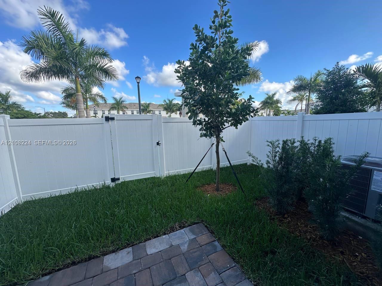 Fenced outdoor area featuring a paver patio, manicured lawn, established landscaping, and a gated entrance