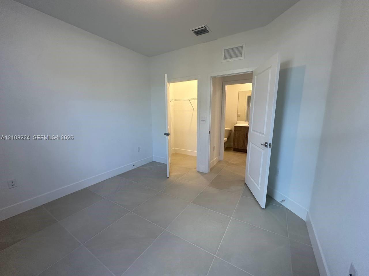 Neutral-toned large-format tile flooring, multi-panel doors, and walk-in closet space Neutral-toned large-format tile flooring, multi-panel doors, and walk-in closet space