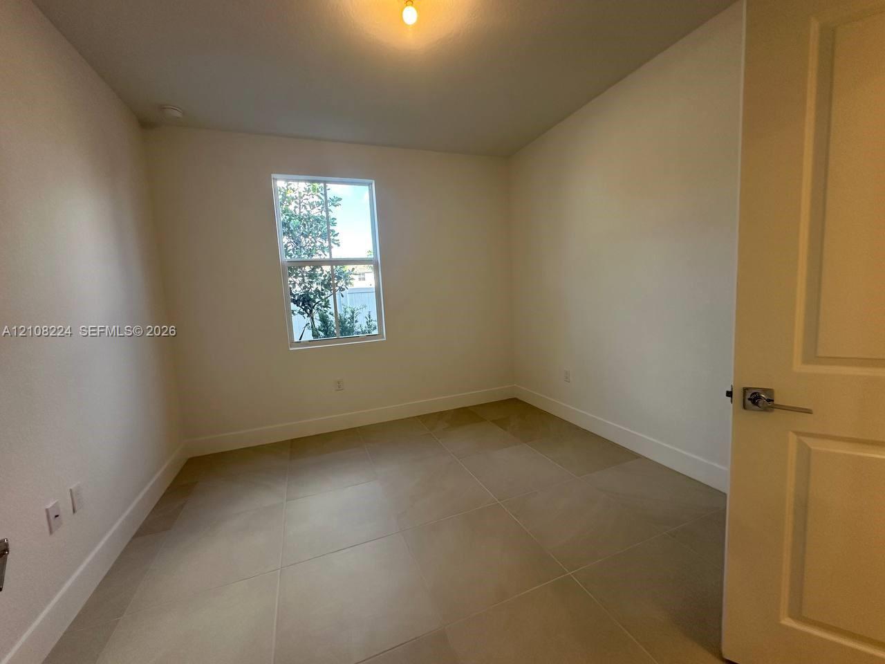Neutral-toned large-format tile flooring, single-hung window, white interior walls, and a multi-panel door with a satin-finish lever handle Neutral-toned large-format tile flooring, single-hung window, white interior walls, and a multi-panel door with a satin-finish lever handle