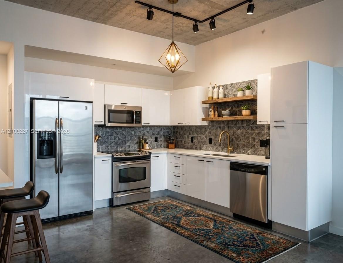 Modern kitchen featuring sleek white cabinetry, stainless steel appliances, patterned tile backsplash, floating wood shelving, and exposed concrete ceiling