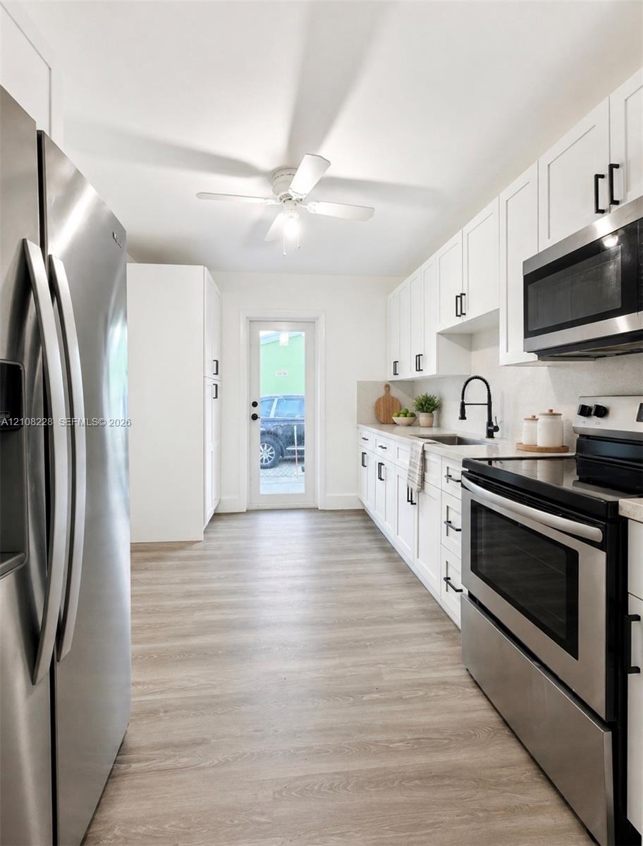 Kitchen featuring white shaker-style cabinetry with matte black hardware, stainless steel appliances, wood-finish flooring, and a glass-paneled exterior door