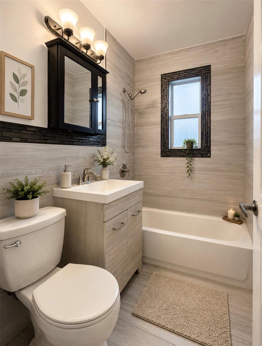 Bathroom featuring horizontal tile wall cladding, wood-finish vanity with an integrated sink, dark-framed medicine cabinet, and a tiled tub surround with a window inset