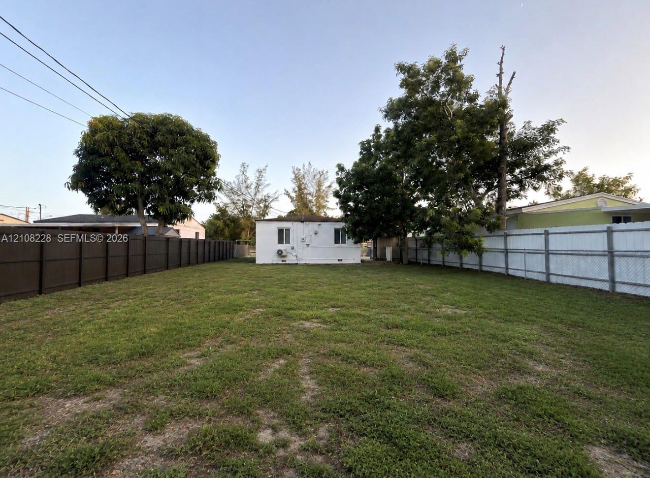 Expansive backyard featuring an open grass lawn, mature trees, and privacy fencing on two sides