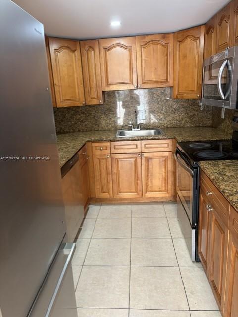 Kitchen featuring wood cabinetry, stone-finish countertops, stainless steel appliances, a double-basin undermount sink, and tile flooring