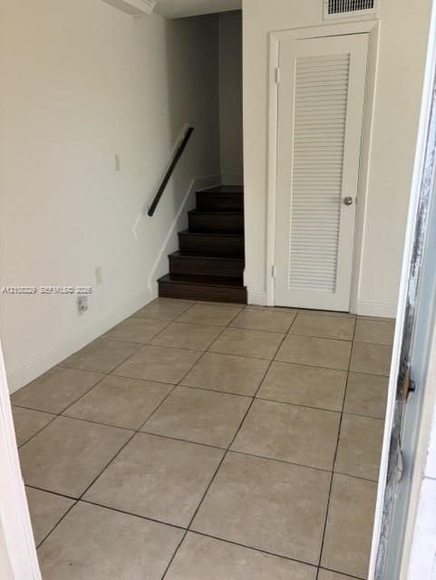 Neutral-toned tile flooring, dark wood-finish staircase, and louvered-panel closet door