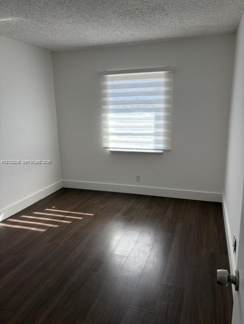 Neutral-toned room featuring dark wood-finish flooring, a single-pane window with zebra-style roller shades, and a textured ceiling finish