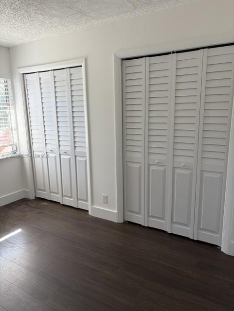 Two built-in bi-fold closets featuring white louvered doors, dark wood-finish flooring, and white window shutters