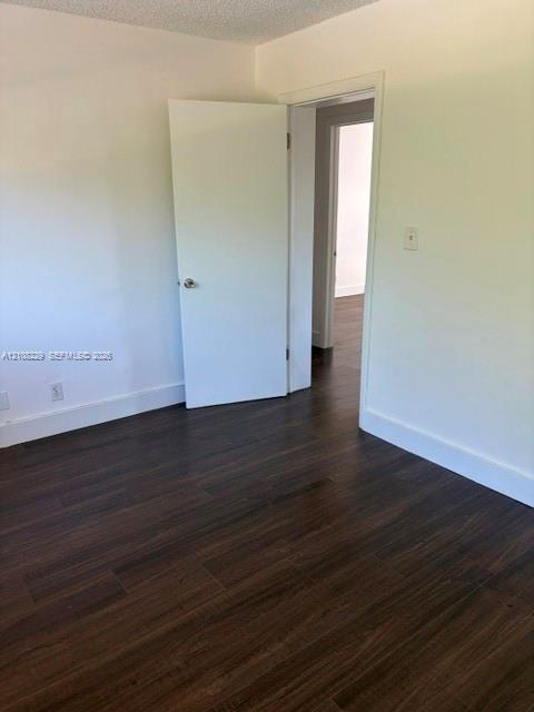 Interior space featuring dark wood-finish flooring, smooth white walls, and a white interior door with a metallic knob