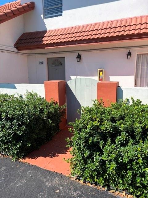 Stucco exterior featuring a terracotta-tiled roof, privacy wall with a gated entrance, and wall-mounted exterior lighting fixtures Stucco exterior featuring a terracotta-tiled roof, privacy wall with a gated entrance, and wall-mounted exterior lighting fixtures