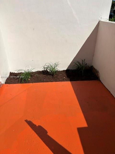 Paved patio featuring terra-cotta colored hardscaping and a dedicated soil garden bed with established ornamental grasses enclosed by smooth white stucco walls