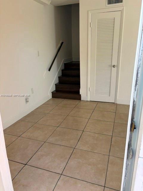 Neutral tile flooring, wood-finish staircase treads, and a classic louvered closet door