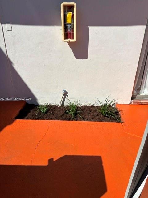 Painted concrete patio featuring a rectangular garden bed with planted greenery and an exterior wall-mounted fire extinguisher cabinet
