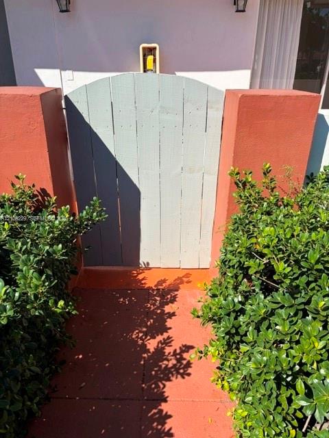 Arched wooden pedestrian gate flanked by stucco-finished masonry pillars and mature greenery