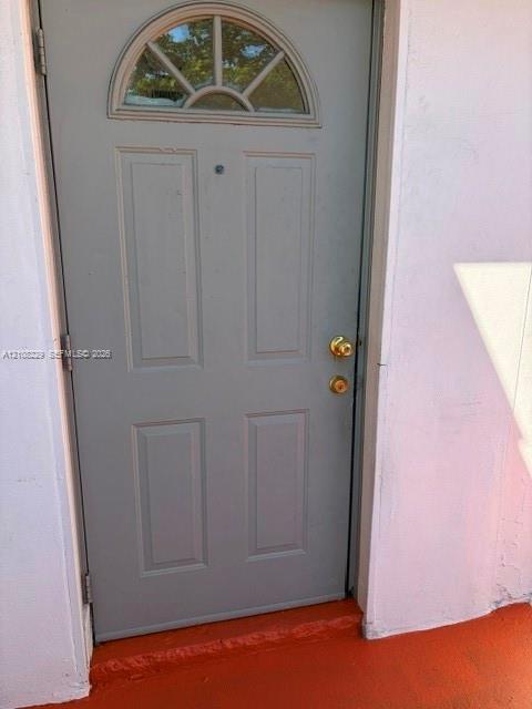 Gray four-panel door featuring a semi-circular transom window, brass-finish hardware, and a door viewer