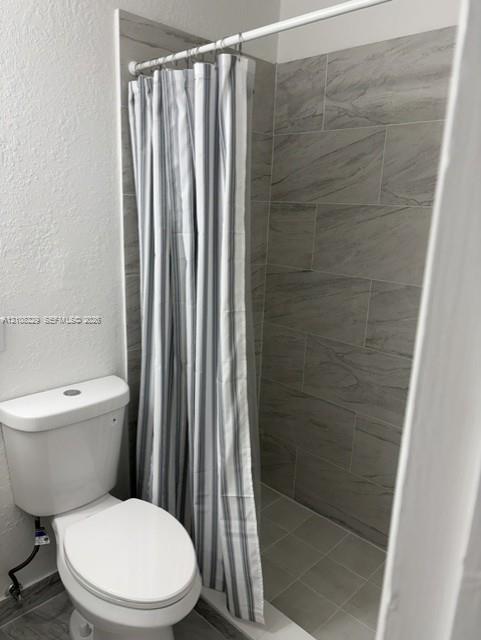 Shower enclosure featuring floor-to-ceiling large-format neutral-toned tile work and a white porcelain commode