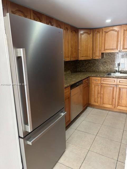Kitchen featuring wood cabinetry, stone-surface countertops, stainless steel appliances, and tile flooring