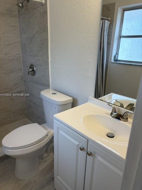 Bathroom featuring a vanity with a white countertop and oval under-mount sink, tile shower surround, and neutral floor tiling