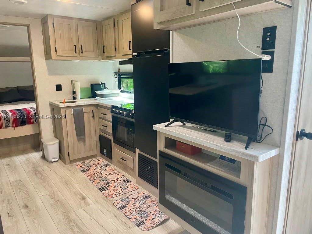 Kitchen featuring light wood-finish cabinetry, countertop with stone-patterned surfacing, integrated oven and stovetop, wood-finish flooring, and a built-in electric fireplace