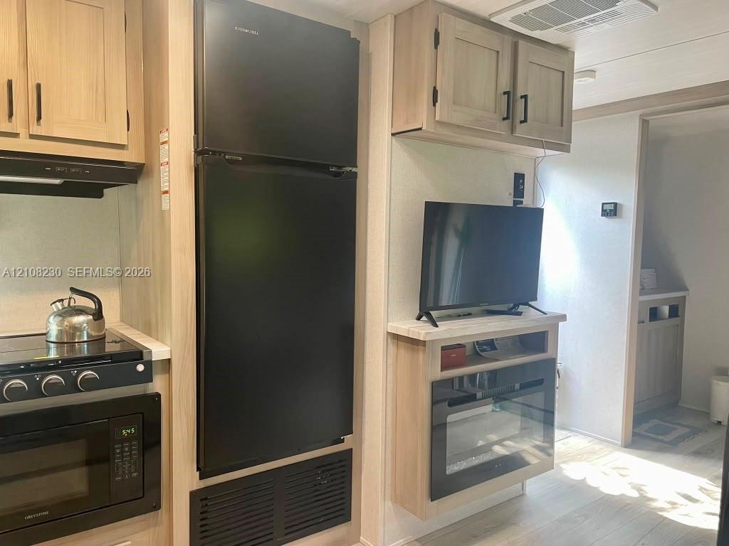 Kitchen area featuring light-toned cabinetry, a black full-size refrigerator, a built-in microwave, and a black cooktop