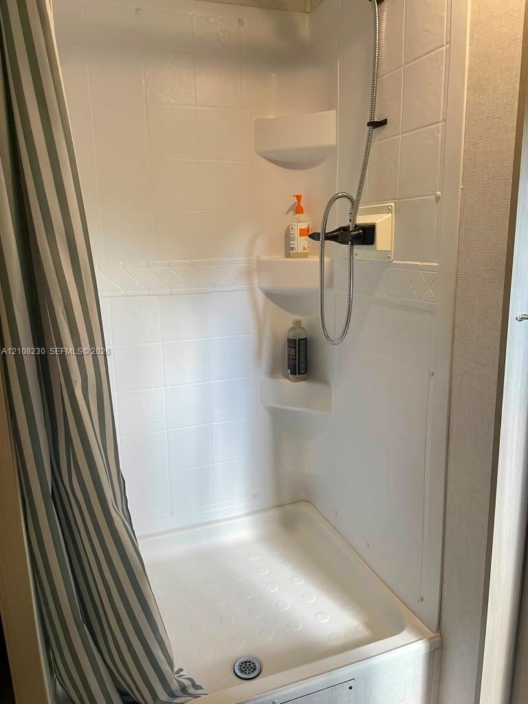 Shower enclosure featuring white wall panels with a textured tile pattern, three integrated corner shelves, a molded shower pan, and a handheld shower fixture