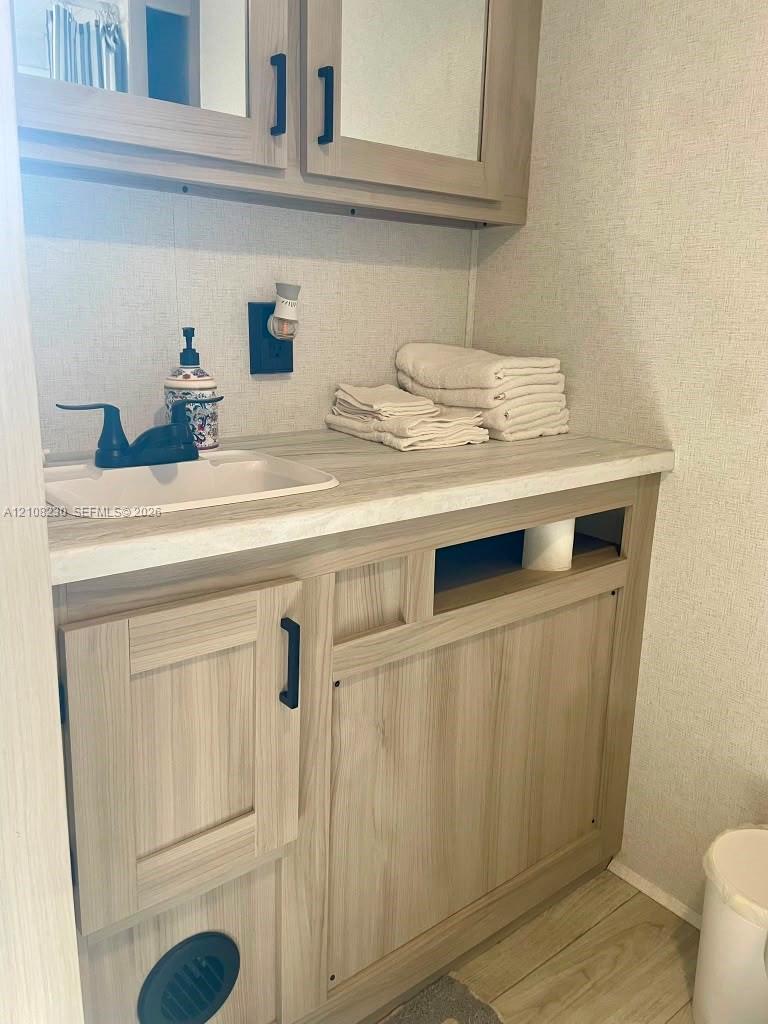 Vanity with wood-finish cabinetry, solid-surface countertop, integrated sink, matte black faucet, and mirrored medicine cabinet