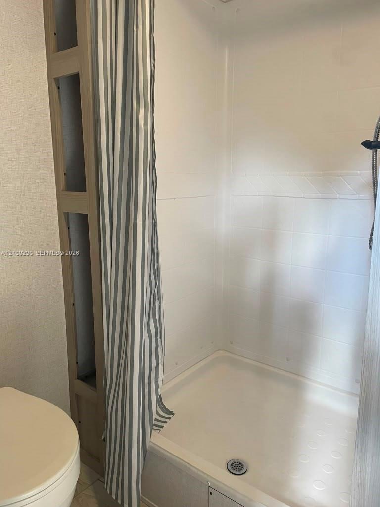 Shower stall featuring a molded composite surround, integrated shelving unit, and handheld shower fixture