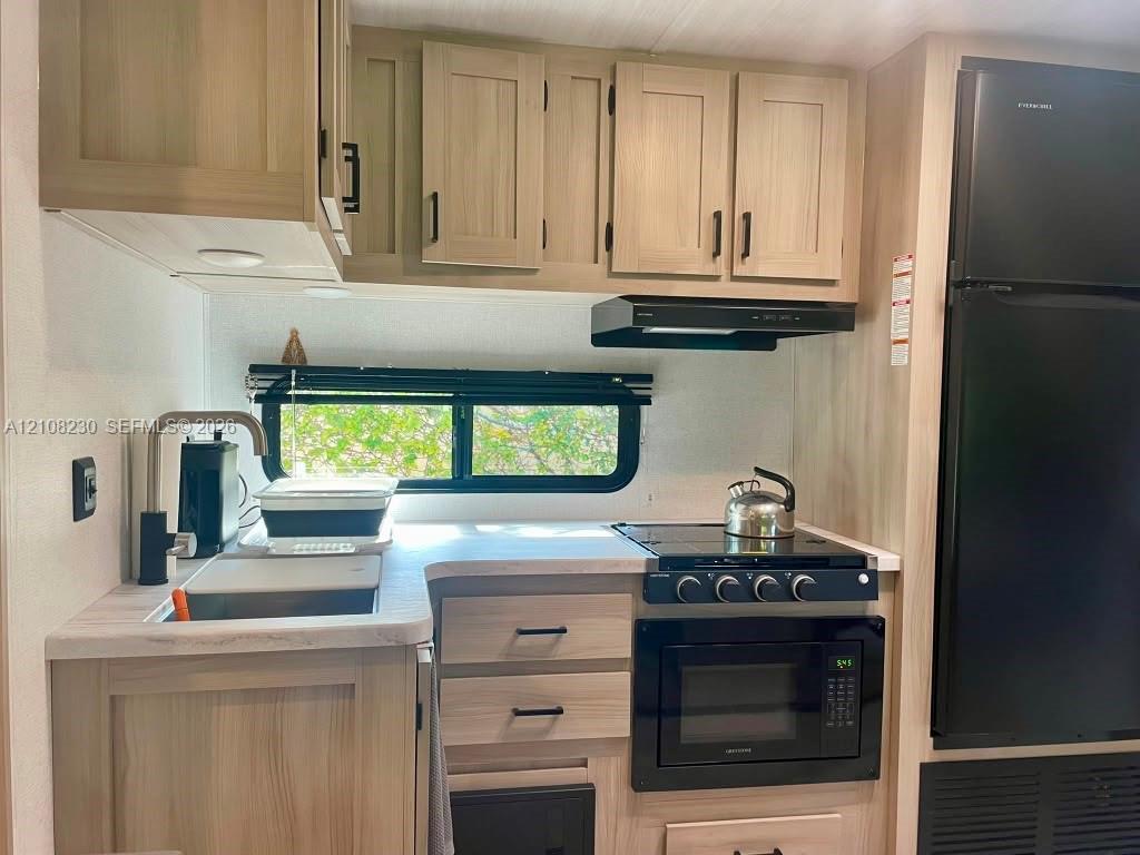 Kitchen featuring wood-finish cabinetry, light-toned countertops, a matte black faucet, and built-in black appliances including a stove, microwave, and refrigerator