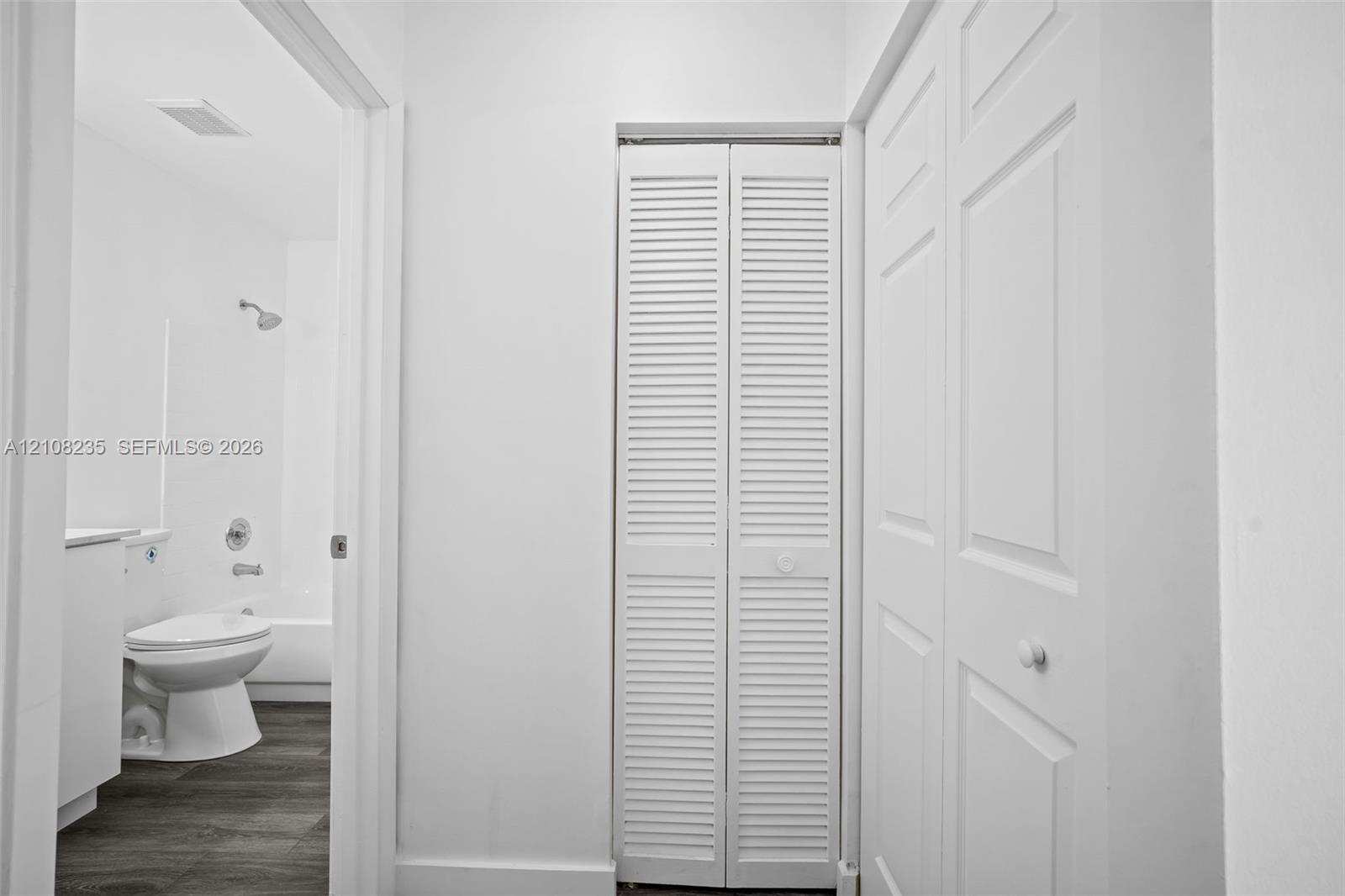 White bifold louvered closet doors, dual-panel interior doors, and wood-finish flooring