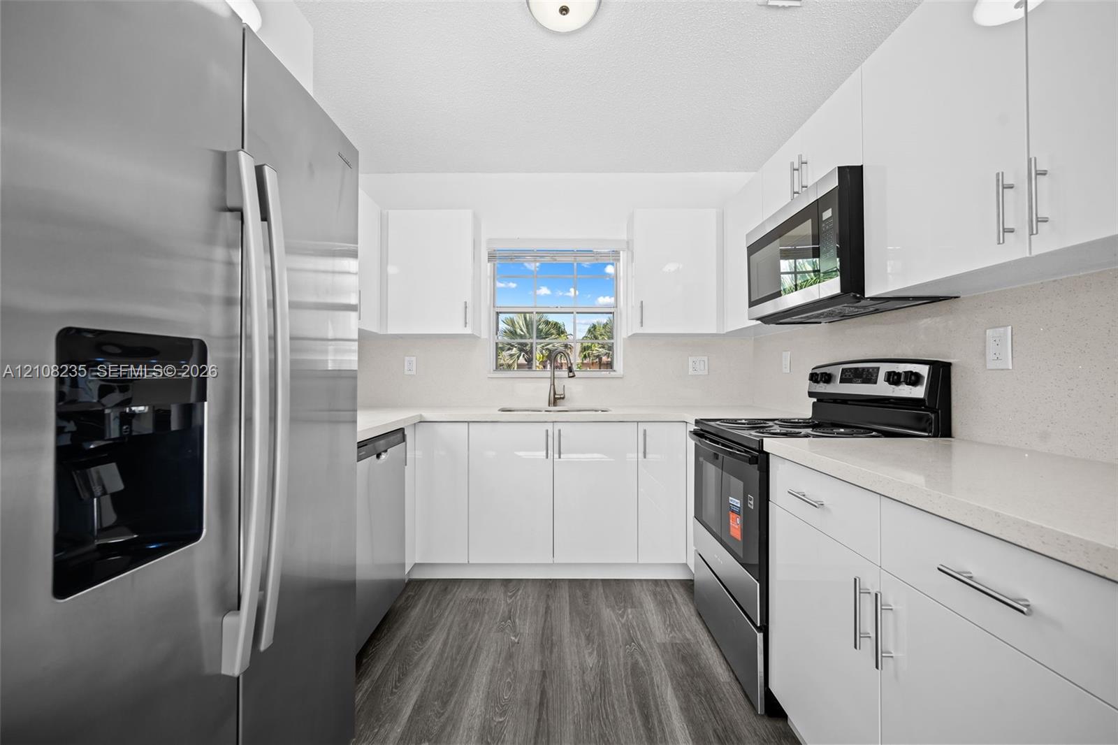Kitchen featuring high-gloss white cabinetry, light-toned stone countertops, stainless steel appliances, and wood-finish flooring