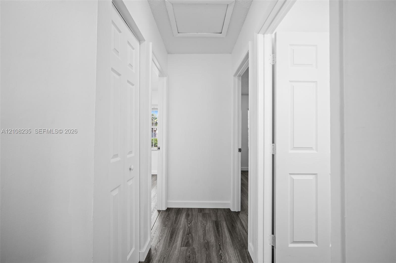 Hallway featuring wood-finish flooring, six-panel interior doors, and a ceiling access panel