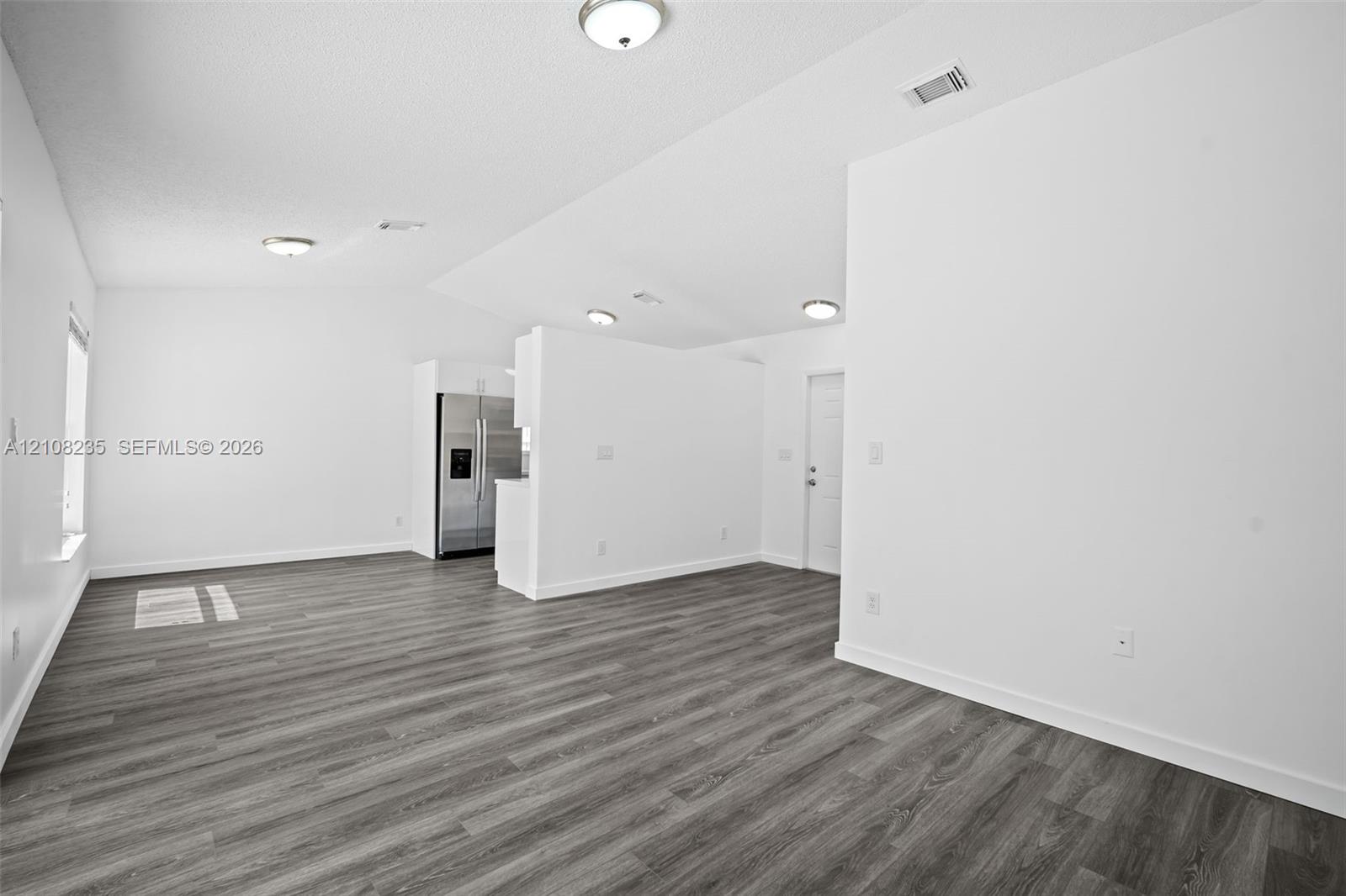 Vaulted ceiling with flush-mount lighting and wood-finish flooring throughout the open-concept space, featuring a stainless steel side-by-side refrigerator