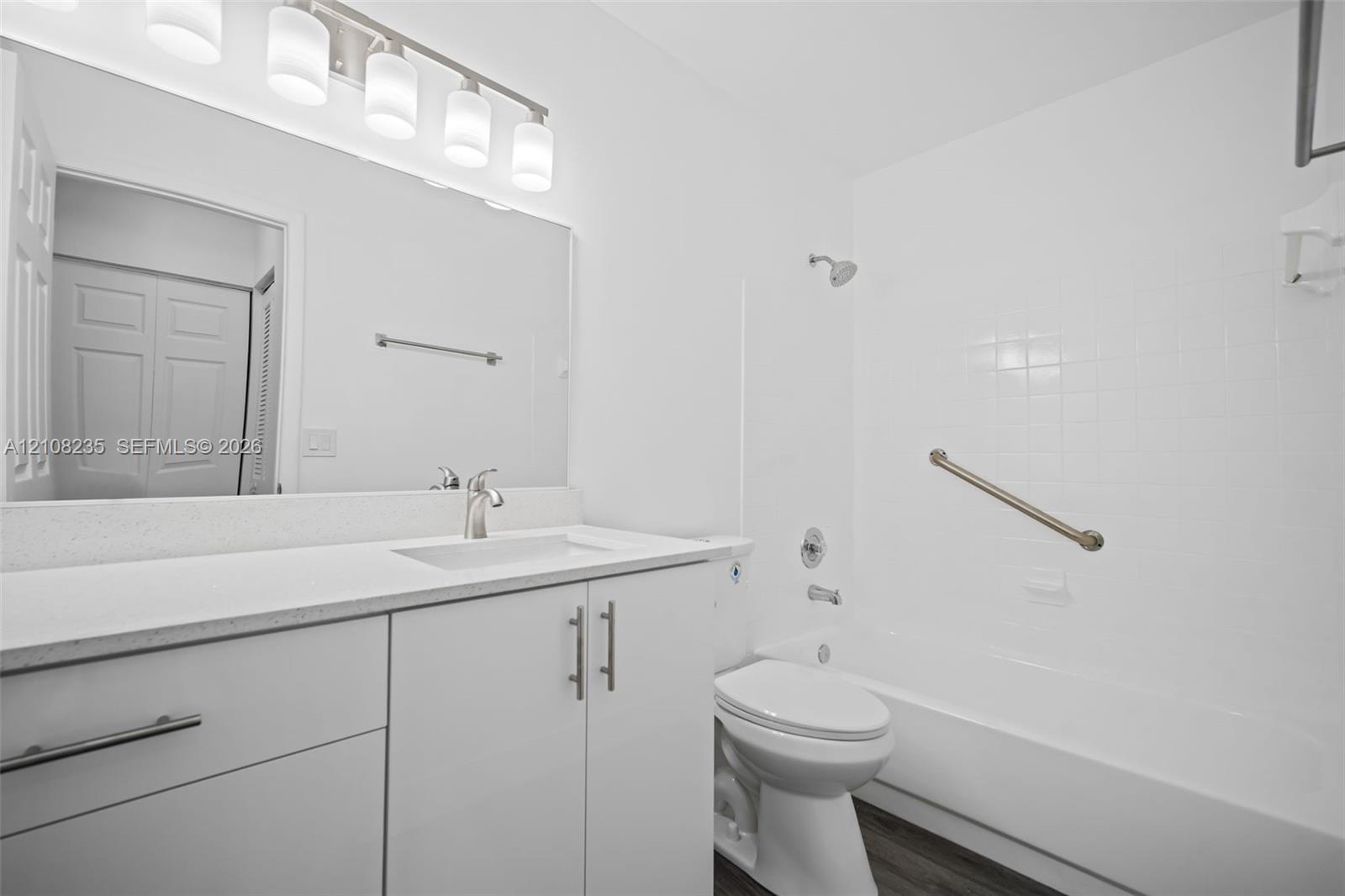 Bathroom featuring a white vanity with a solid surface countertop, an integrated sink, a full-width mirror, five-light overhead fixture, and a tile-surround shower and tub combination