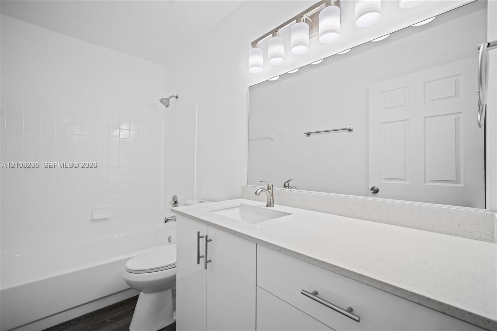 Bathroom featuring a white vanity cabinet, solid surface countertop with an integrated basin, full-width vanity mirror, five-light fixture, and a tub-shower combination with tile surround