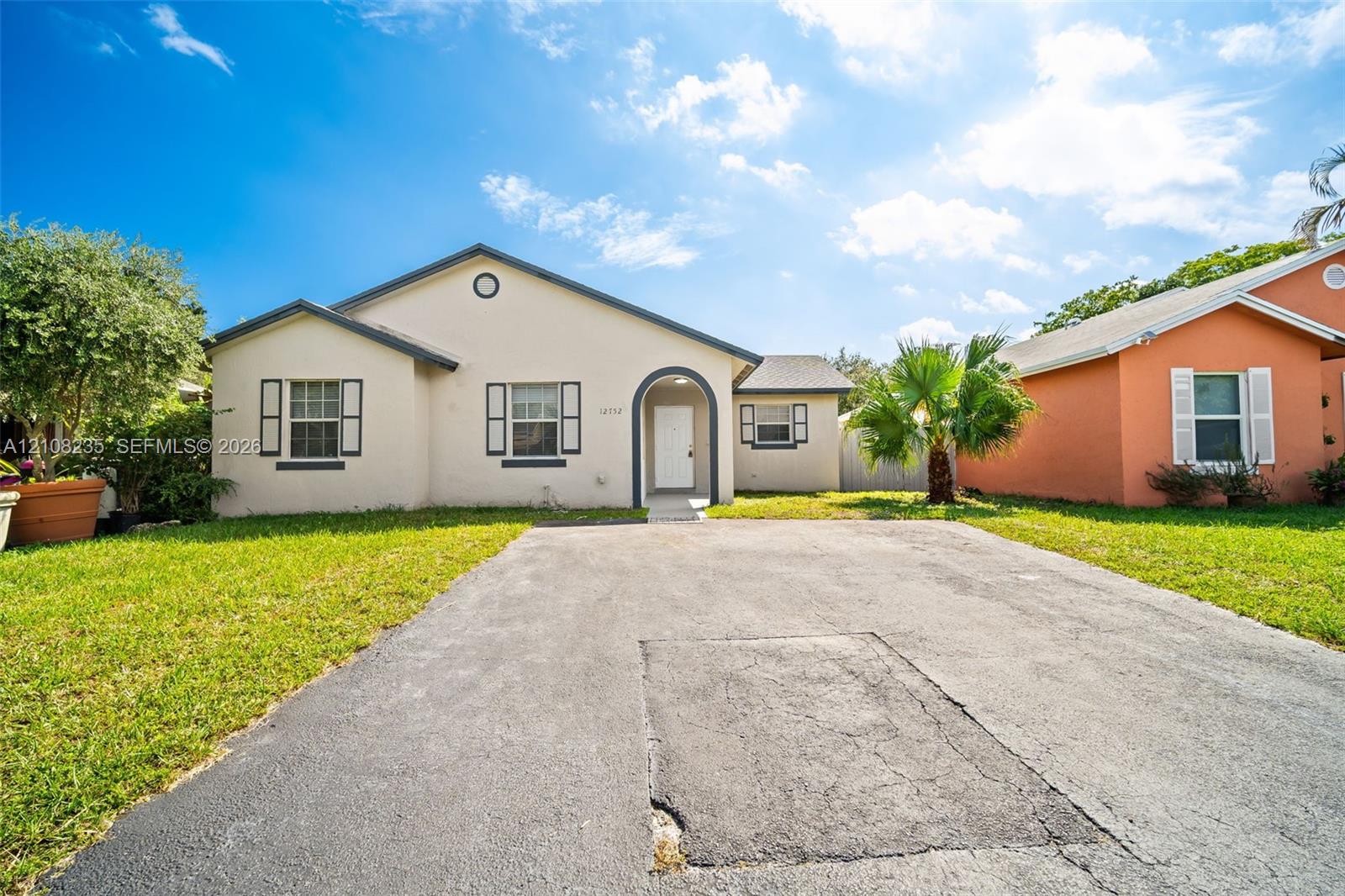 Single-story stucco exterior featuring an arched entryway, decorative shutters, and an asphalt driveway