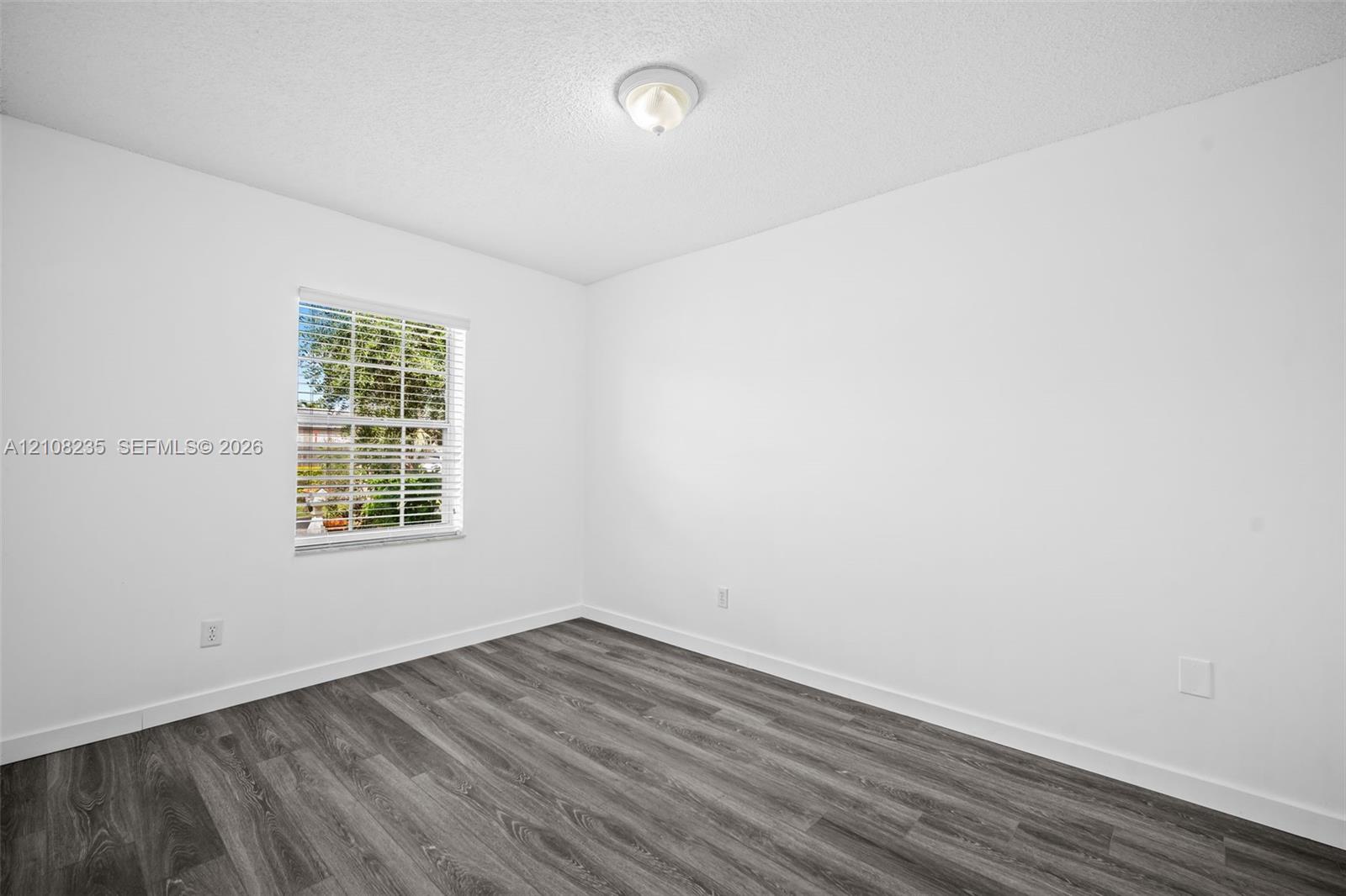 Room featuring wood-finish flooring, white walls, and a window with horizontal blinds