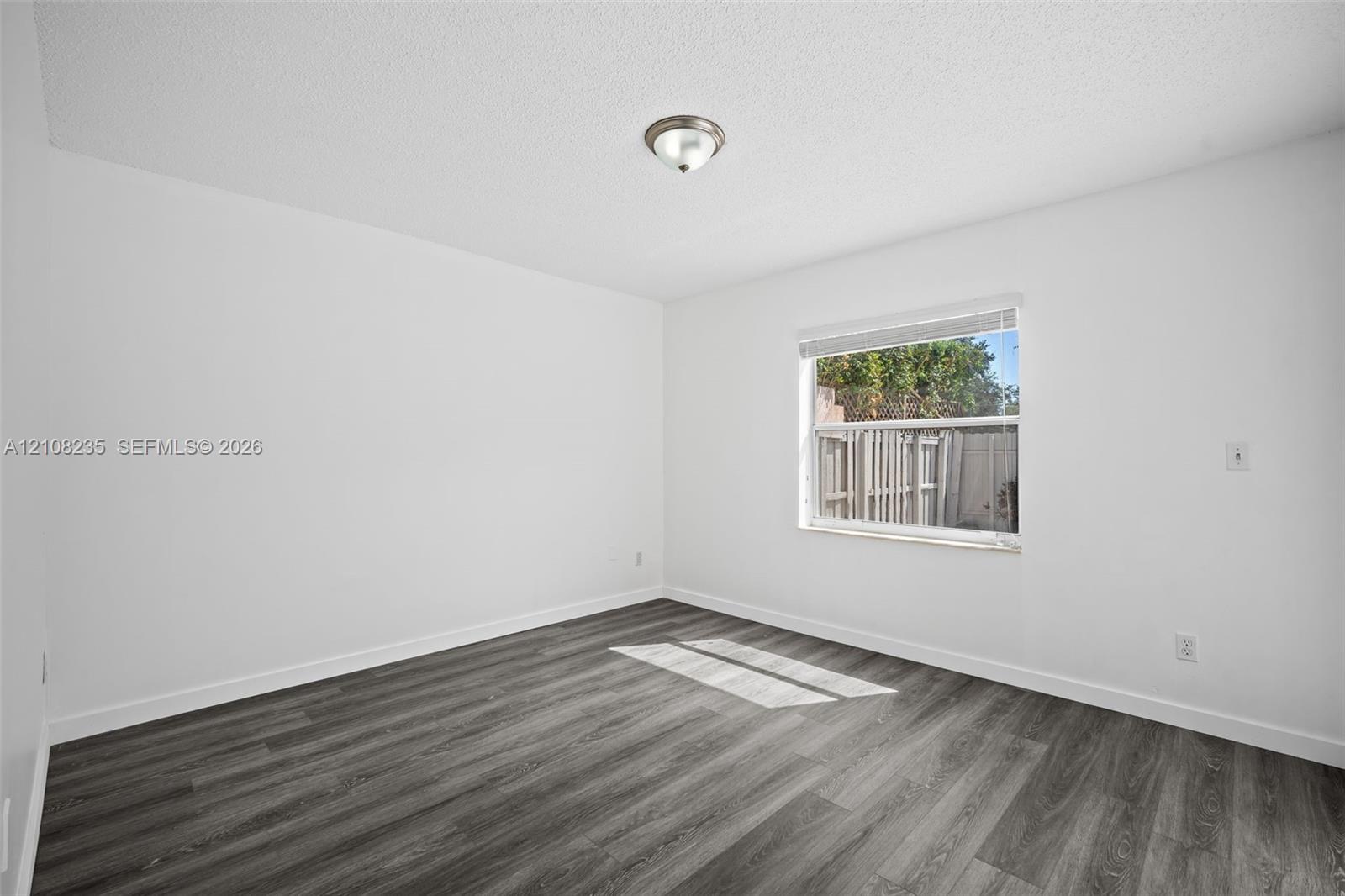 Room featuring wood-finish flooring, a single-pane window with white horizontal blinds, and a flush-mount ceiling light fixture