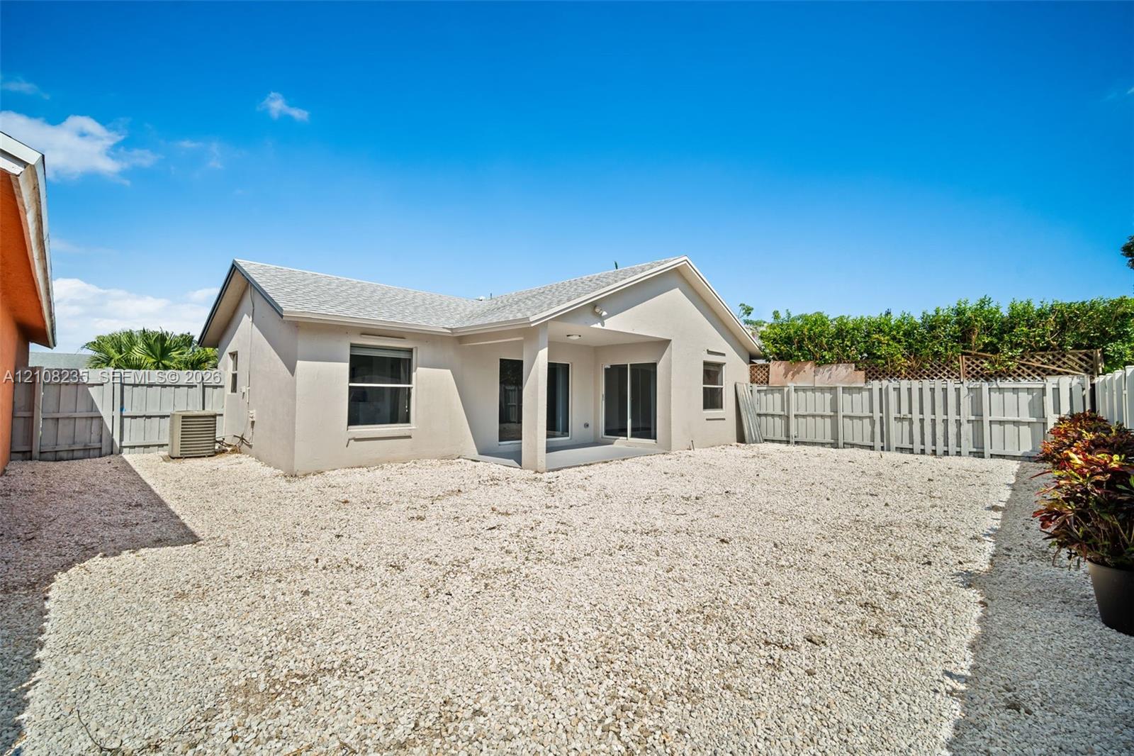 Exterior view featuring a covered patio, neutral-toned stucco siding, a gravel-surfaced yard, and privacy fencing
