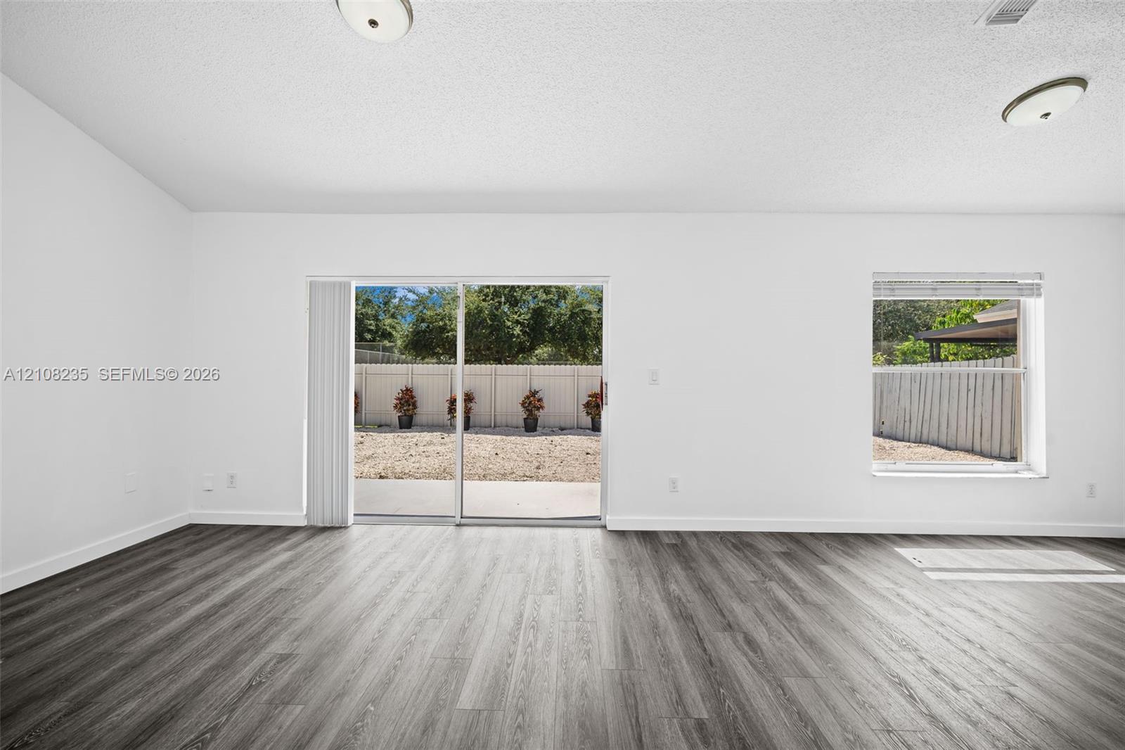 Interior space featuring wood-finish flooring, vaulted ceilings, dual flush-mount light fixtures, and a sliding glass door providing access to the rear exterior