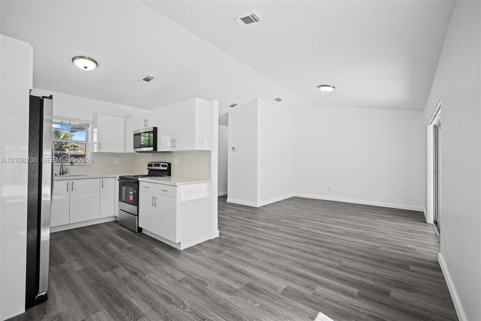 Kitchen featuring white cabinetry, solid-surface countertops, stainless steel appliances, and wood-finish flooring