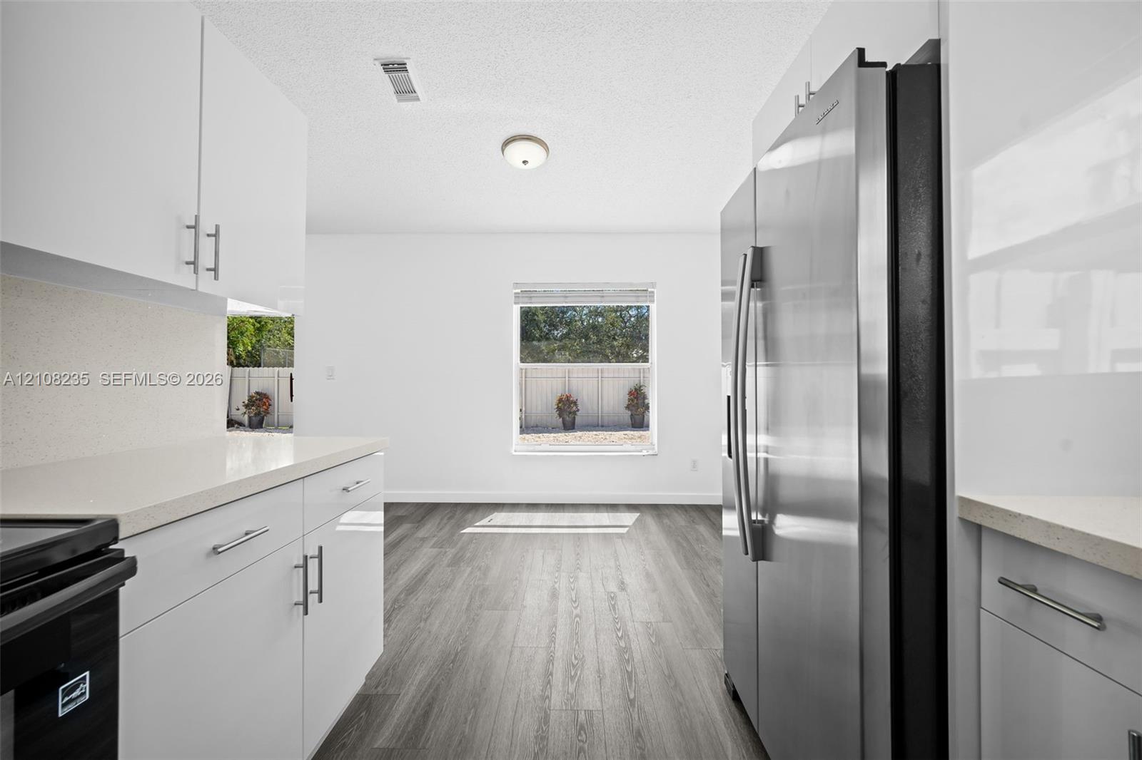 Kitchen featuring white flat-panel cabinetry, light-toned stone-surface countertops, wood-finish flooring, and a stainless steel side-by-side refrigerator