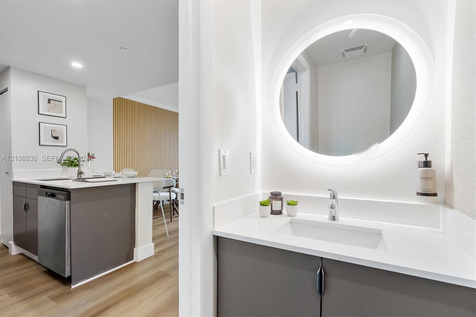 Vanity featuring a white countertop with an integrated rectangular sink, matte-finish cabinetry, and a circular wall-mounted mirror with integrated perimeter lighting