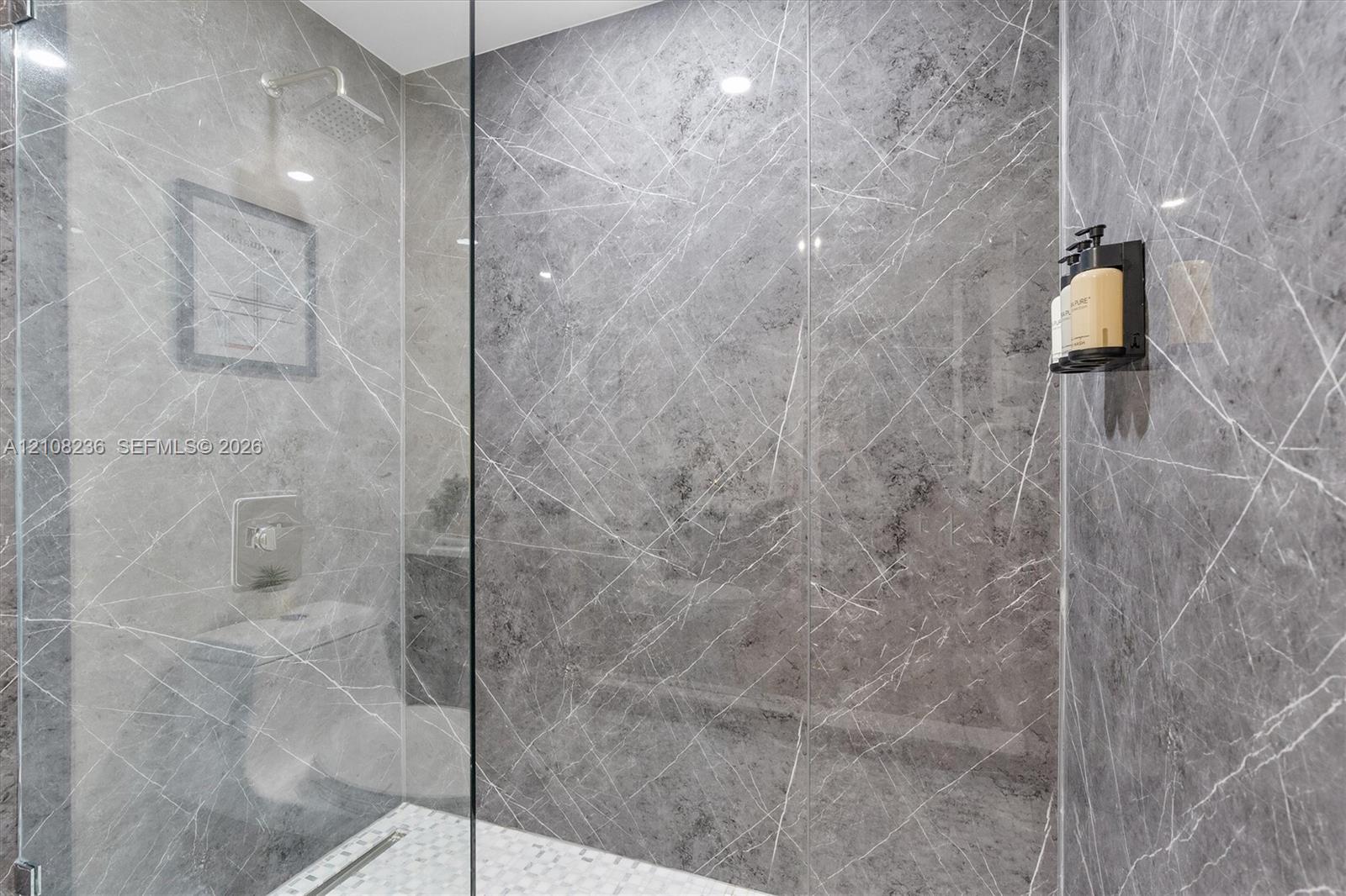 Walk-in shower featuring large-format grey veined tile wall surfacing, frameless glass enclosure, ceiling-mounted rainfall showerhead, and mosaic tile flooring