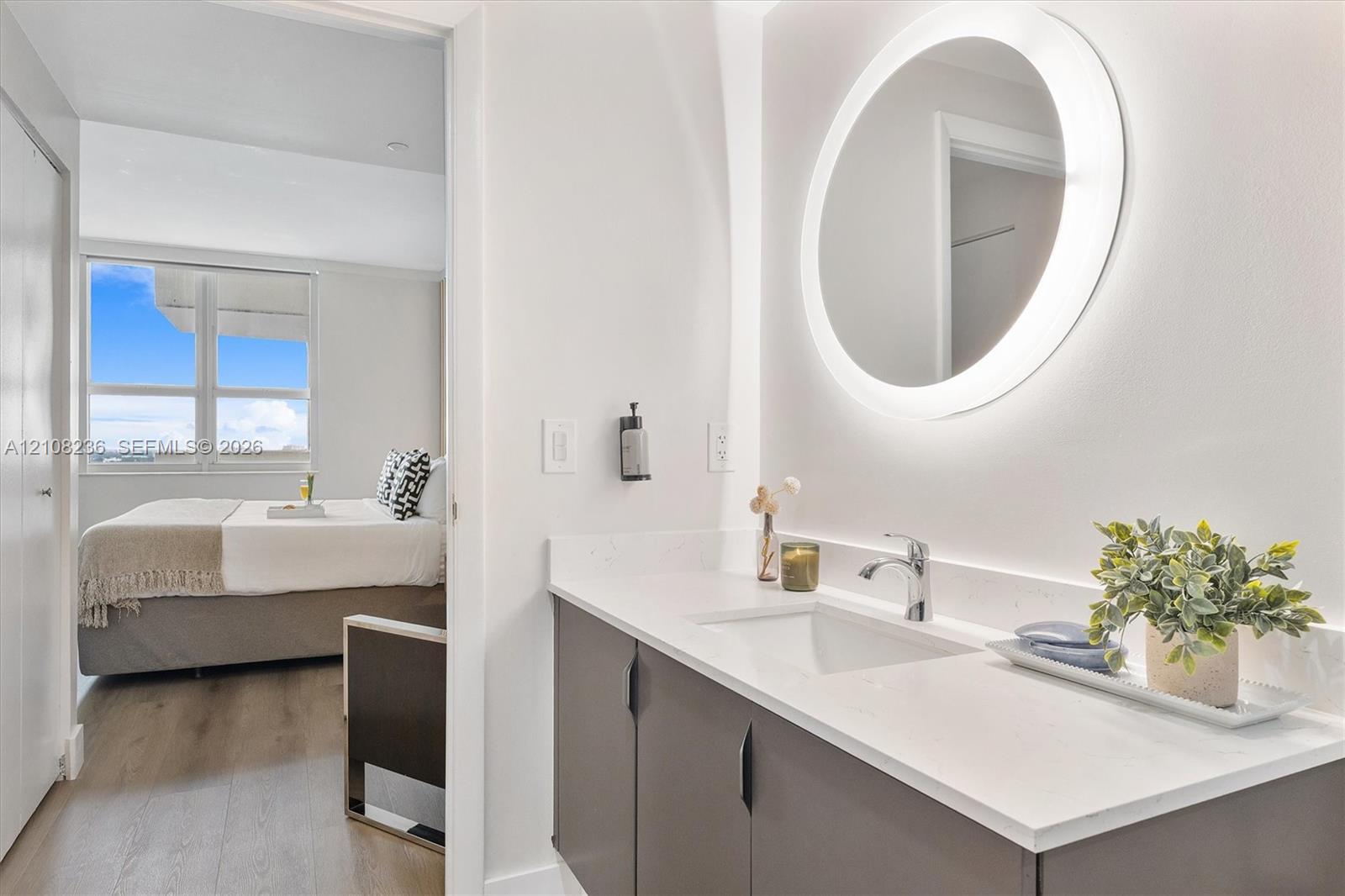 Bathroom vanity featuring a quartz countertop, integrated sink, matte dark cabinetry, and a circular LED-backlit mirror
