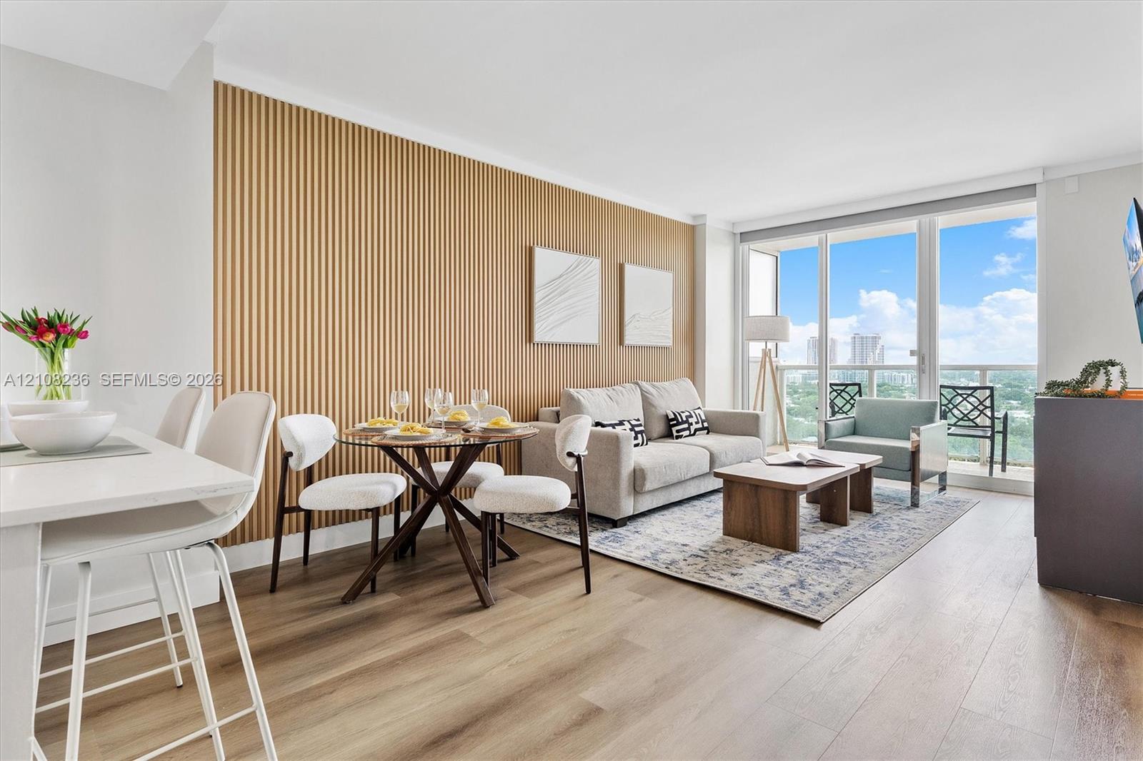 Living area featuring a vertical wood-slat accent wall, wood-finish flooring, floor-to-ceiling glass sliding doors, and an outdoor balcony