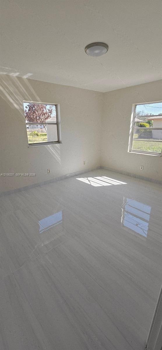 Neutral-toned interior space featuring light-colored tile flooring, smooth walls, two windows, and a circular flush-mount ceiling light fixture