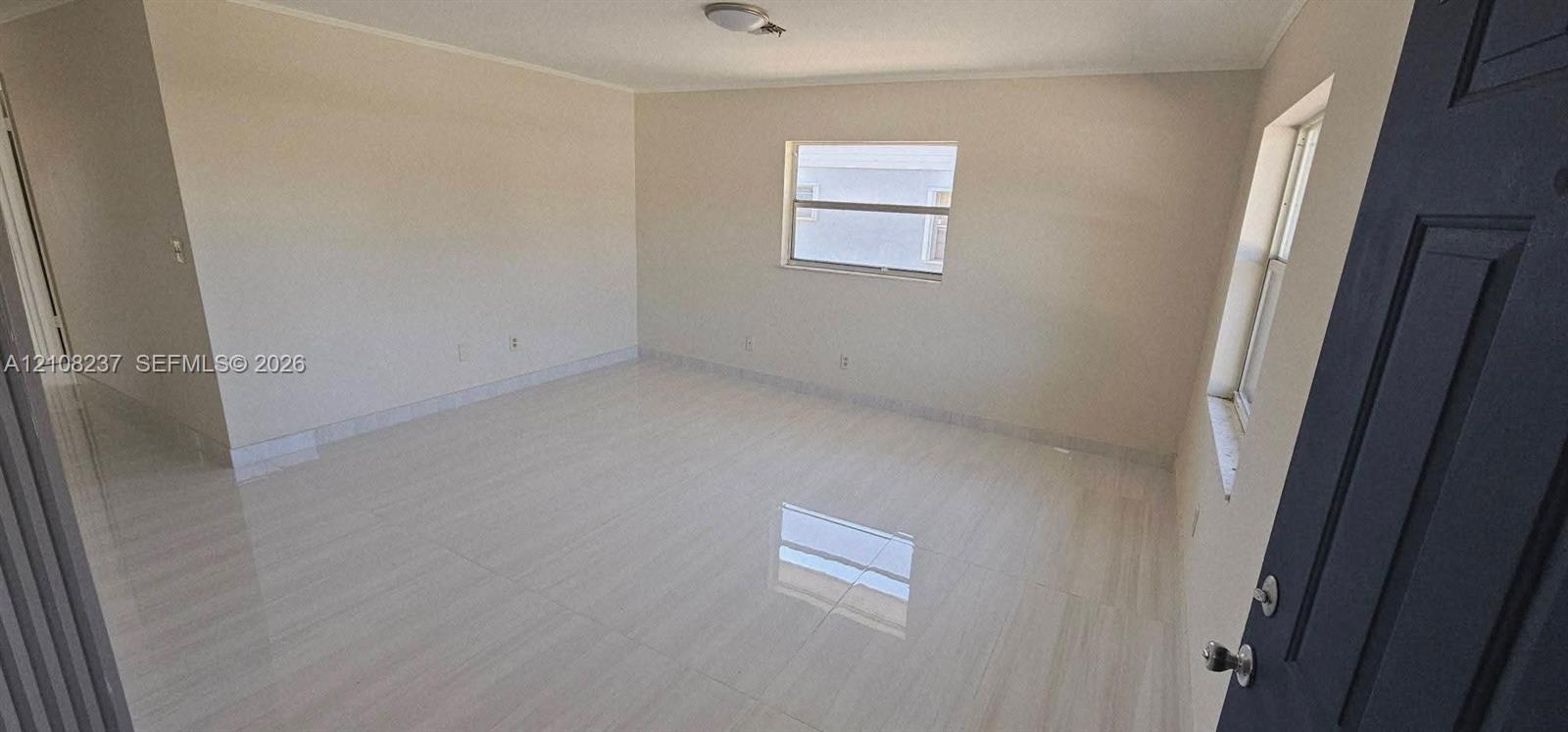 Interior space featuring light-toned tile flooring, neutral wall paint, two single-hung windows, and a multi-panel door with metallic hardware