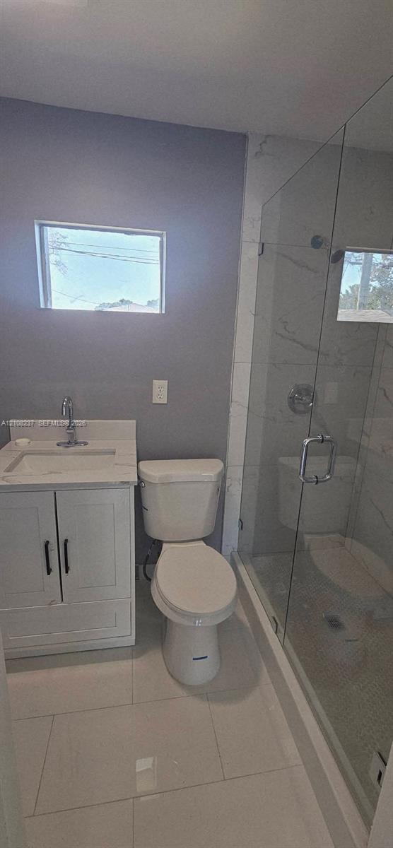 Bathroom featuring a white vanity cabinet with a stone-top integrated sink, polished chrome faucet, glass-enclosed shower with tiled walls, and large-format porcelain tile flooring