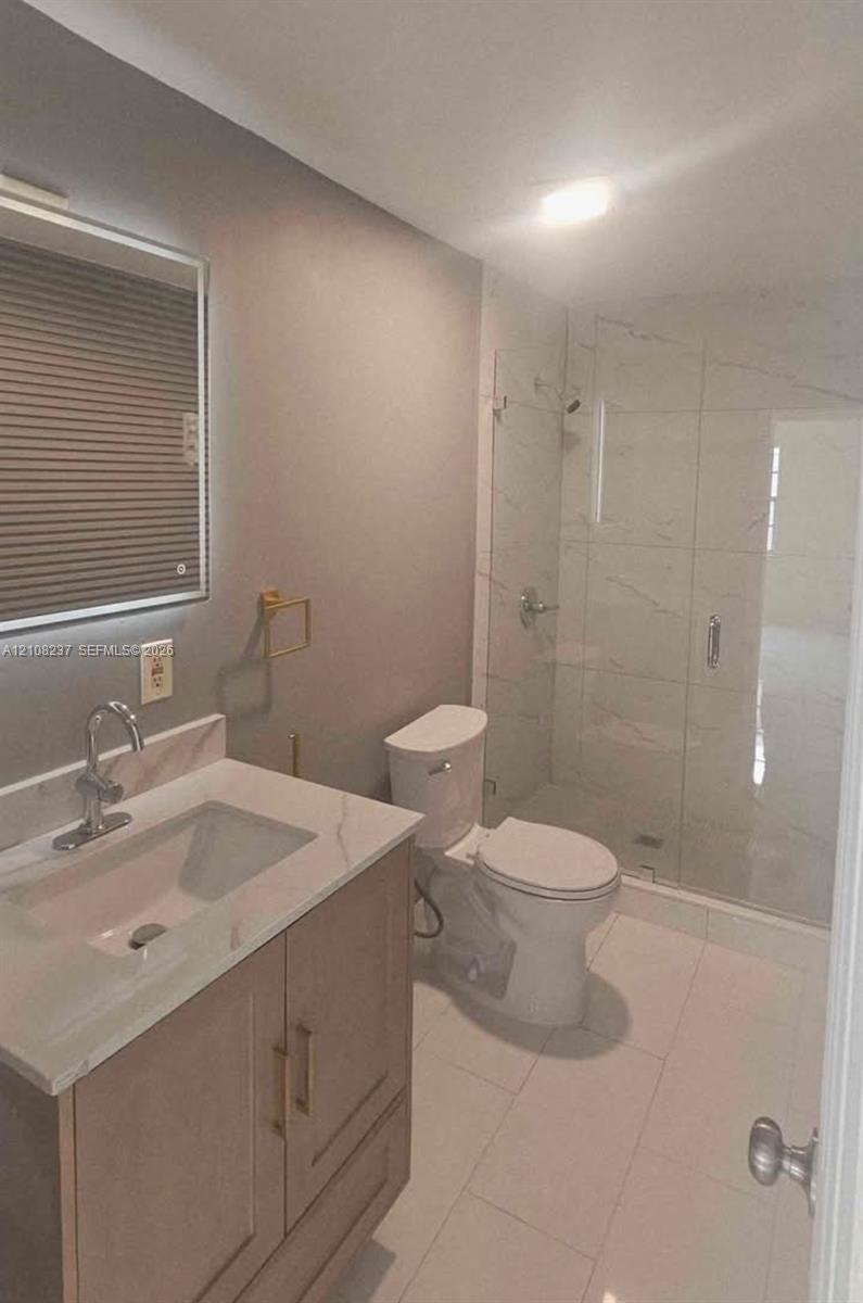 Bathroom featuring a wood-finish vanity with a stone-top integrated sink, wall-mounted mirror, walk-in shower with glass enclosure, and large-format tile flooring