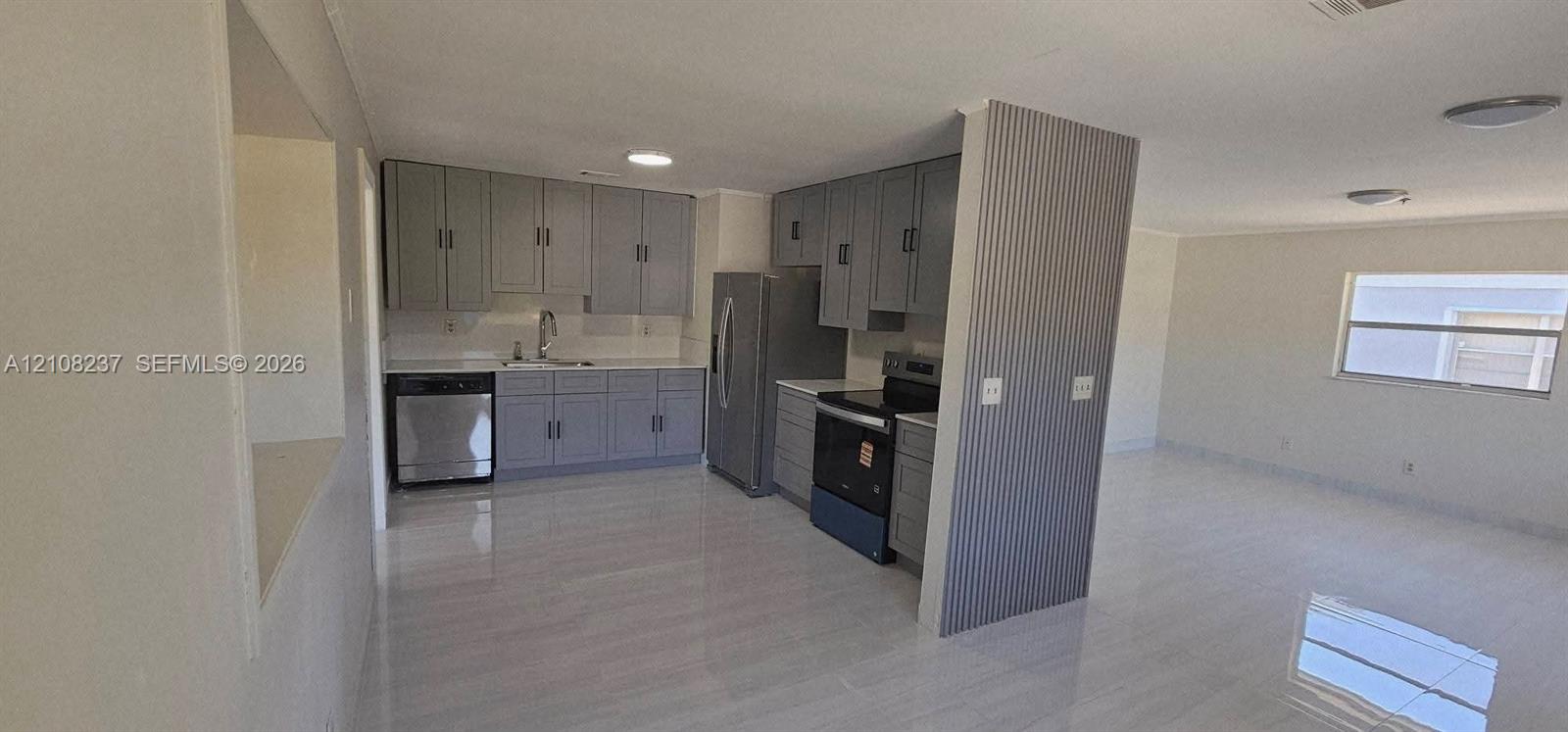 Kitchen featuring grey cabinetry, stainless steel appliances, neutral stone-finish tile flooring, and a decorative corrugated metal accent wall