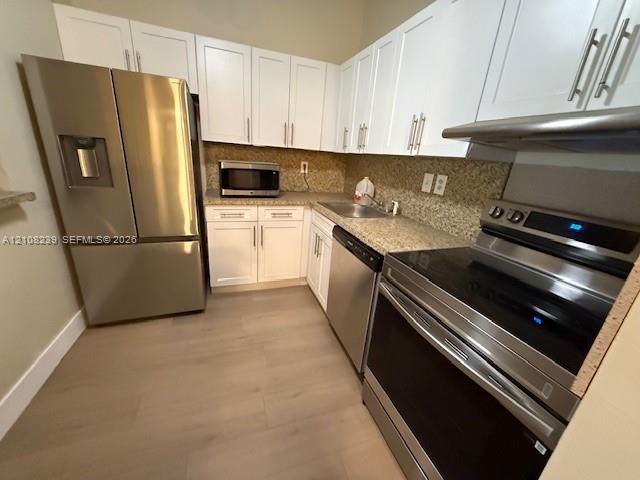 Kitchen featuring white shaker-style cabinetry, stone-finish countertops, stainless steel appliances, and wood-finish flooring